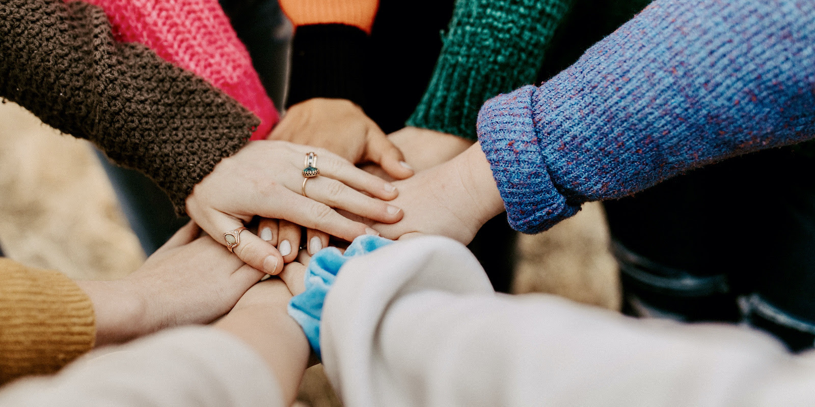 A colorful photograph of people in sweaters putting their hands together at center.